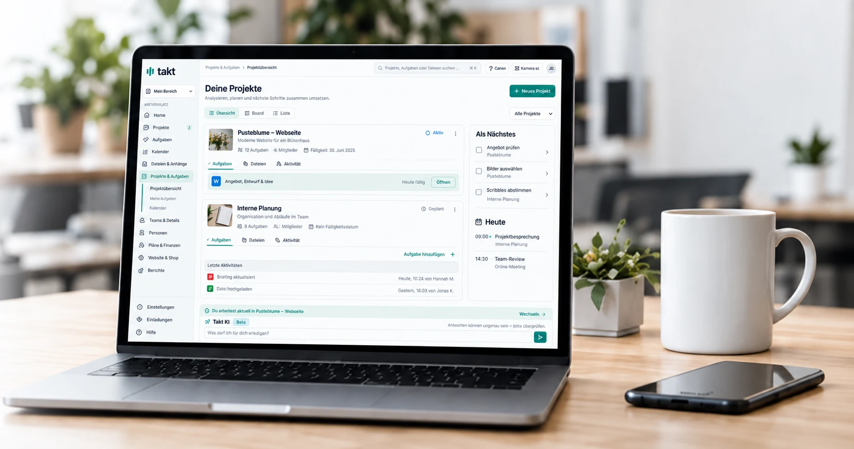Heller Arbeitsplatz mit Laptop und Takt-Projektübersicht, Smartphone und unbeschrifteter Tasse